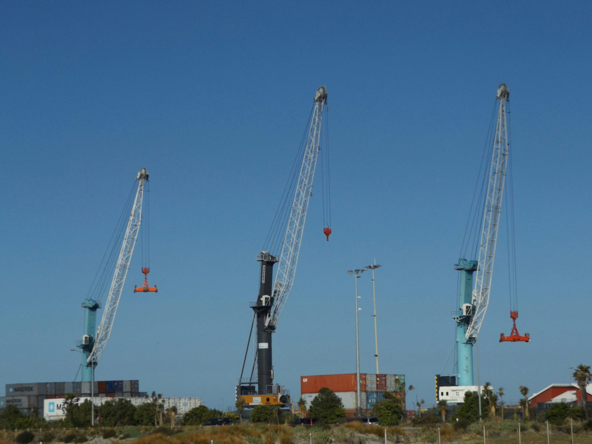 Drei große Industriekräne vor einem klaren blauen Himmel